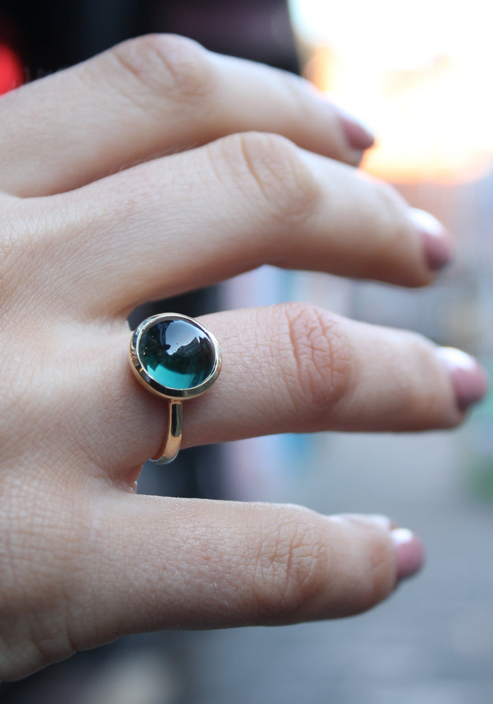 9ct yellow gold ring with a round dark green tourmaline cabochon in a bezel setting. The 9ct yellow gold band is D shaped widest at the back at 3mm wide. Shown here on a ring finger.