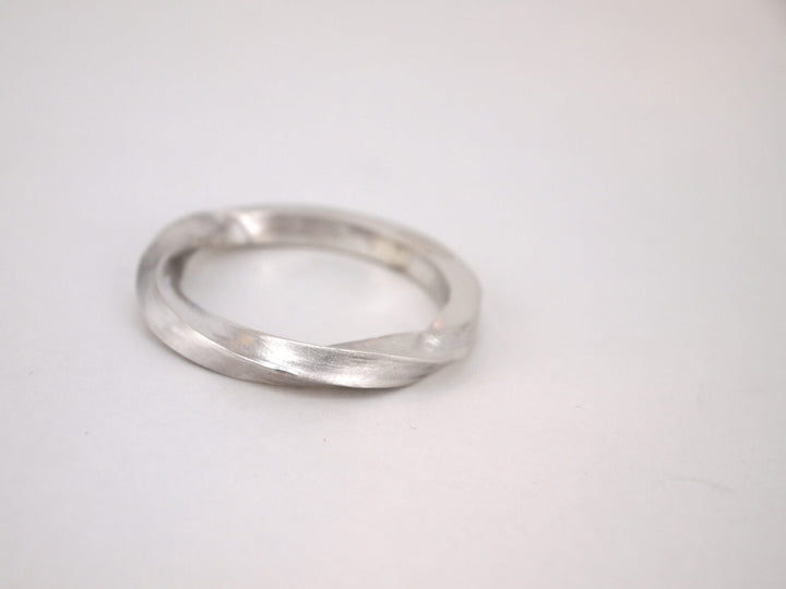 The Torn Silver Ring by MarCucurella is a minimalist handmade piece with a subtle twist design, displayed on a plain white background.