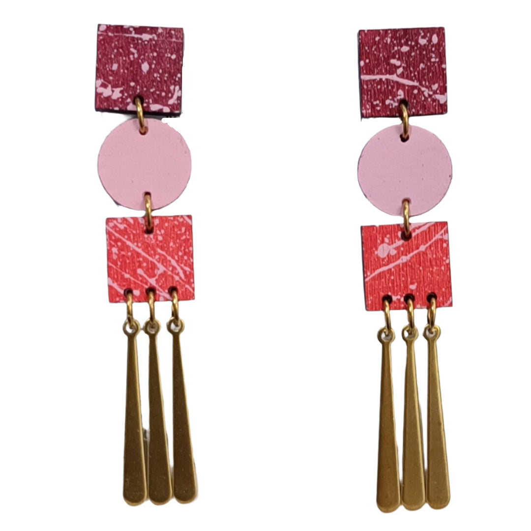 The Trio Grande Earrings in Red & Pink by Shock of Grey feature handcrafted maroon and red squares, a pink circle, and three gold teardrop charms on each earring—a geometric, colorful design inspired by Dublin jewelry trends.