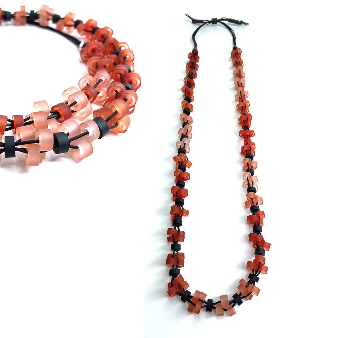 A long, hypoallergenic Alex + Svet Verona Long Necklace handcrafted in Paris, featuring interlocking translucent beads in a gradient from red to peach. The beads are artfully clustered and threaded onto a black cord, with a close-up inset showcasing the detailed bead arrangement.
