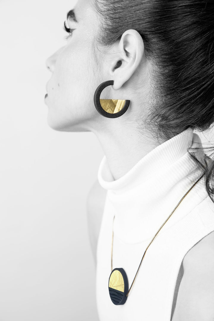 A woman in a sleeveless white turtleneck wears Elsiem’s Vibe Wave Circle Fascia Necklace. She faces left with her hair pulled back, highlighting the bold, modern jewelry.