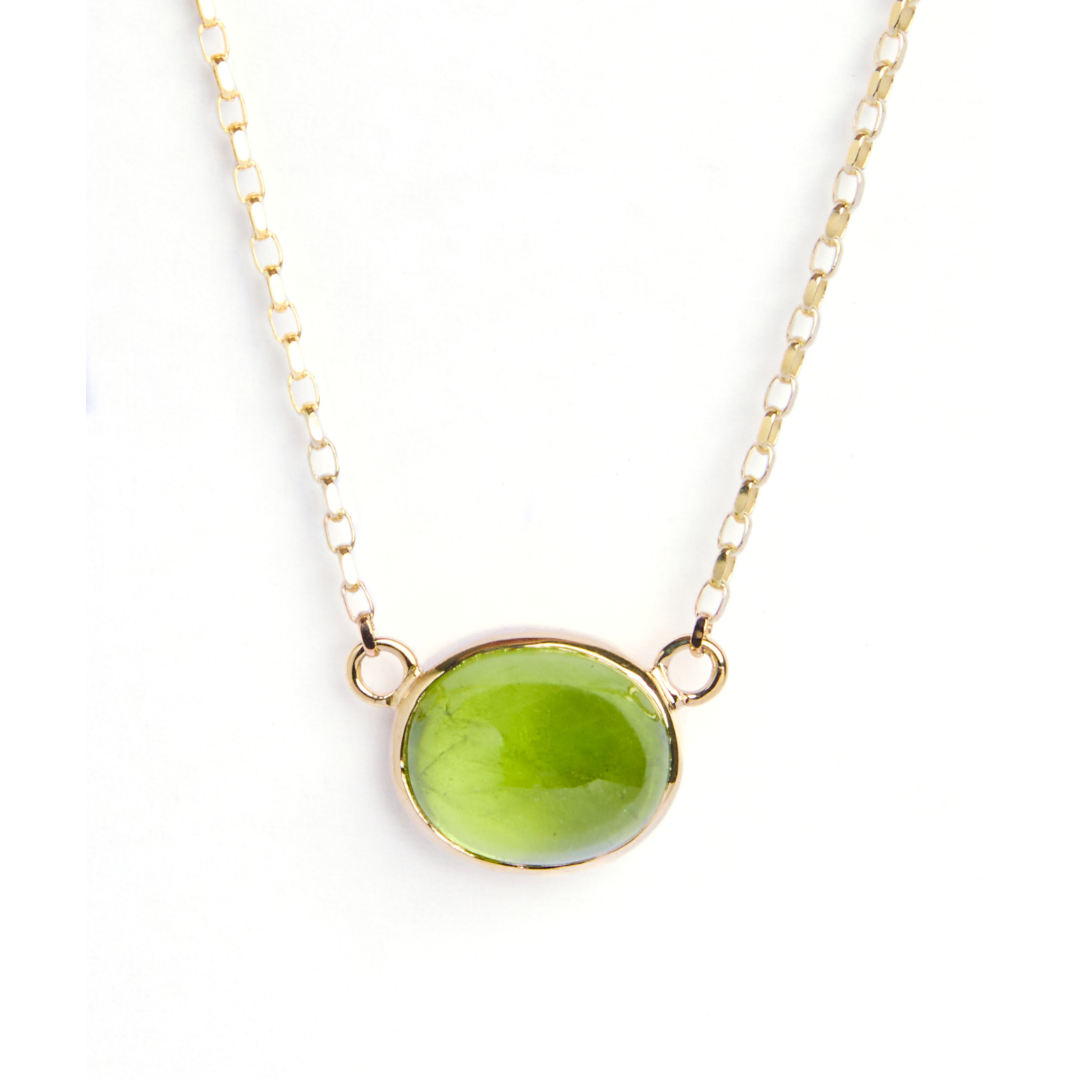 The Madeleine Whispering Moss 9ct yellow gold necklace showcases an oval cabochon peridot pendant in an elegant gold bezel, displayed on a white background.