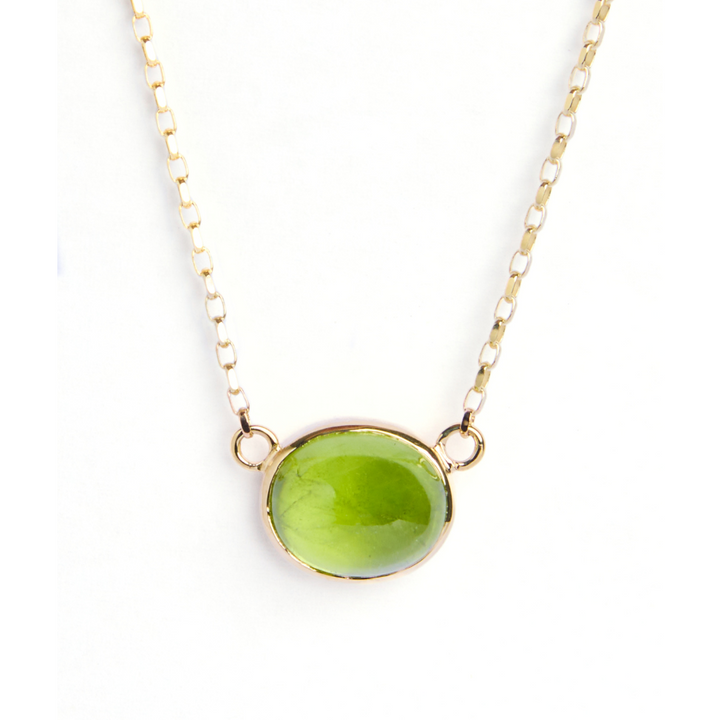 The Madeleine Whispering Moss 9ct yellow gold necklace showcases an oval cabochon peridot pendant in an elegant gold bezel, displayed on a white background.