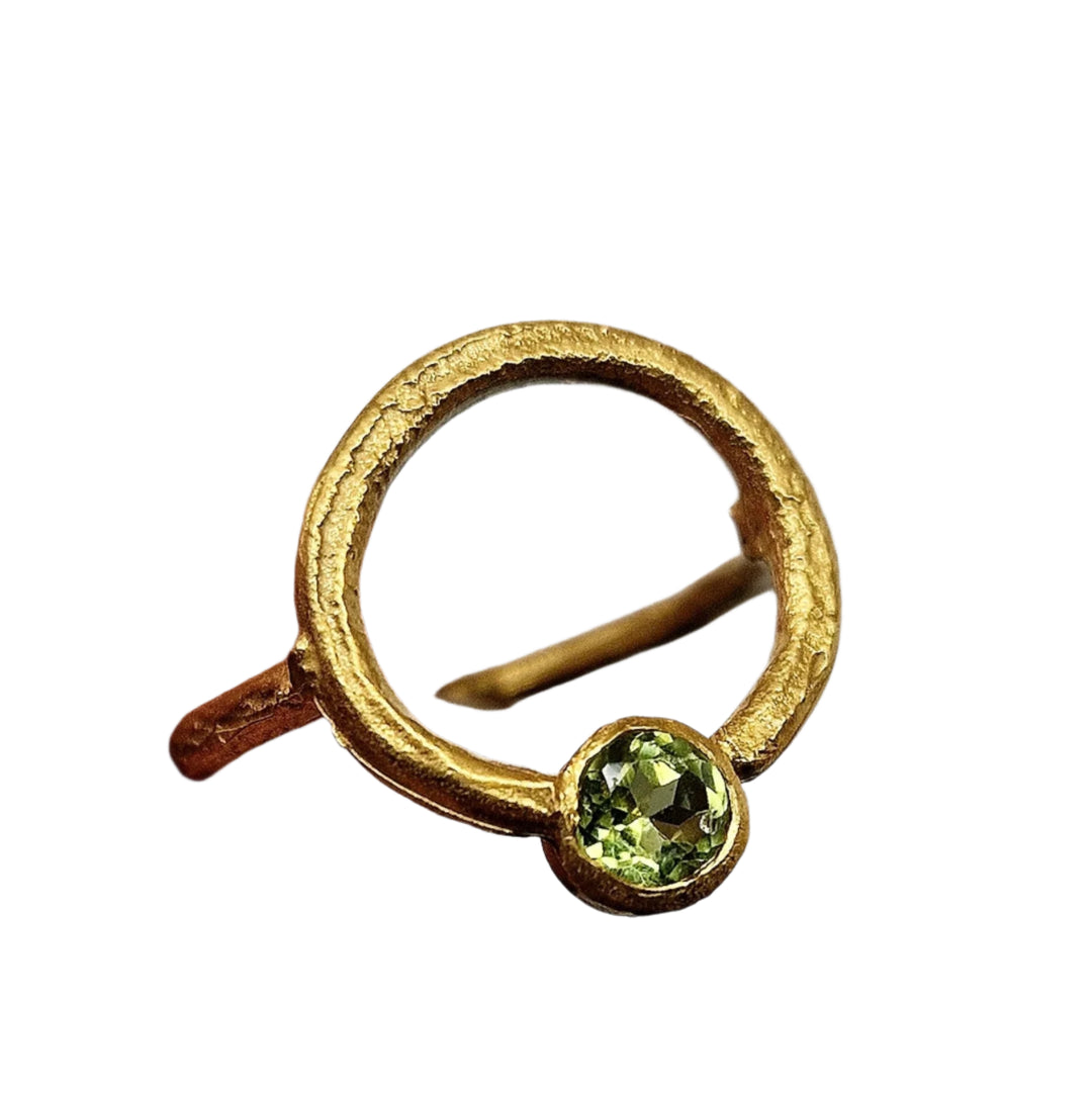 The Peridot Circle of Light Gold Ring by Caroline Stokesberry-lee features a yellow gold plated silver open band with a rough texture and a single peridot at the base, shown on a white background.