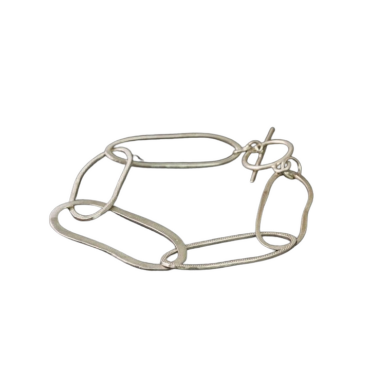 The Drift Bracelet by Lynsey de Burca is a hand-forged sterling silver link bracelet featuring large, interconnected oval links. This minimalist and modern design includes a toggle clasp closure, with one end set in a straight bar and the other in a circular loop. Custom sizing available for the perfect fit.
