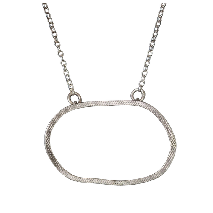 A Lynsey de Burca Drift Pendant Silver, a hand-forged silver necklace with a thin, irregularly-shaped oval pendant suspended from a chain with small round links. The textured sterling silver pendant adds subtle detail to its minimalist design. Its simple elegance makes it an understated accessory.