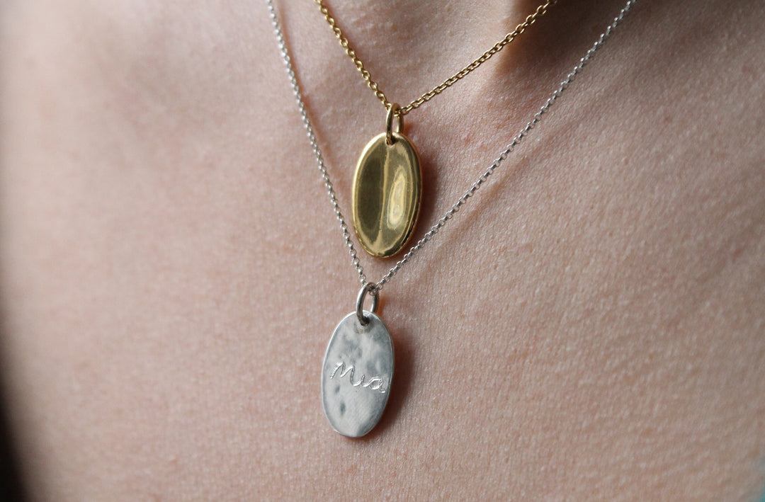 A necklace with an organic oval shaped pendant with a small indent on the front.