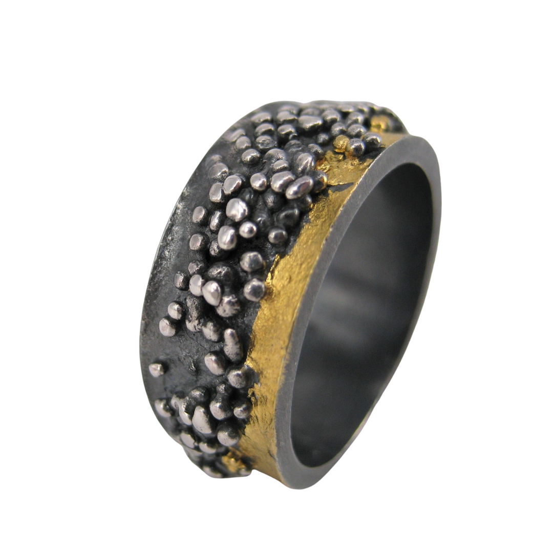 The MarCucurella Wide Etrusc Ring features a textured black and silver surface with Etruscan-style raised silver dots and an uneven gold band running through the center.