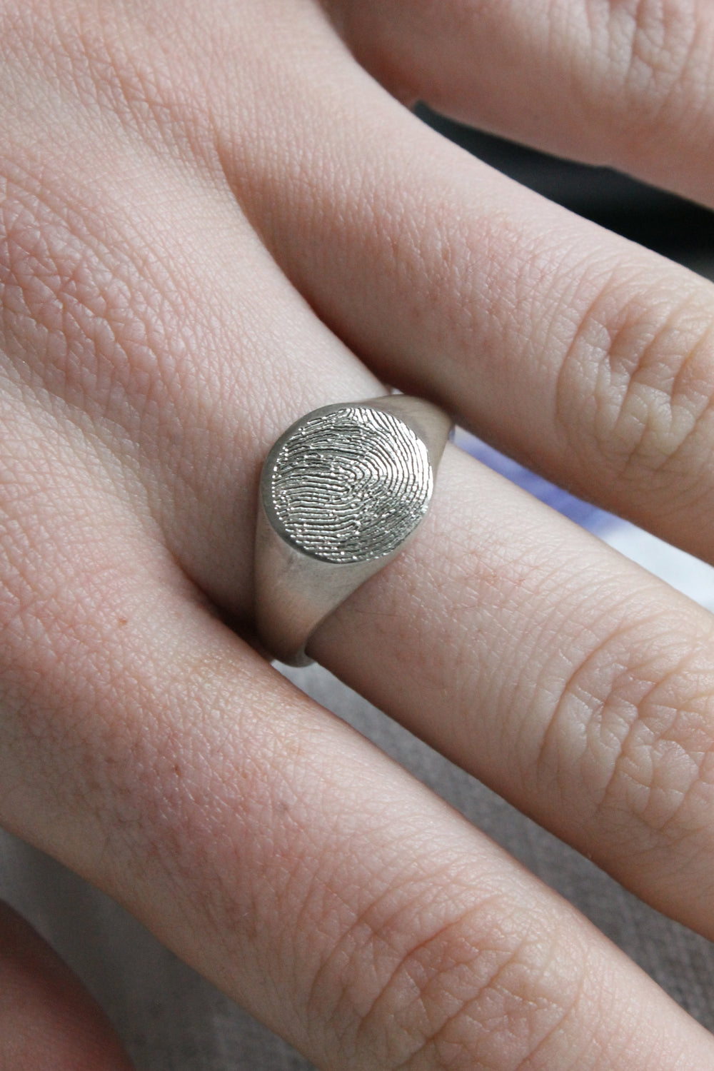 A close-up of a hand wearing the Personalised Charms Engraved Fingerprint Sterling Silver Round Signet Ring, showcasing its unique fingerprint design.