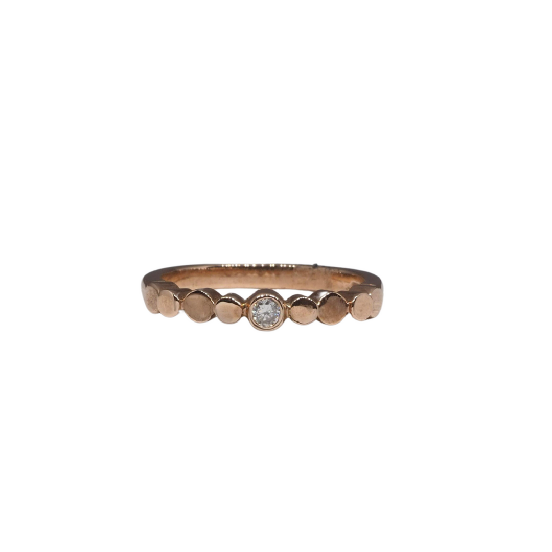 A delicate Flow Pebble Ring 9ct Rose Gold with Diamond by Miriam Wade features a small, central diamond. The band is adorned with evenly spaced circular gold accents. This made-to-order design is simple yet elegant, highlighting the single diamond in the center against a plain white background.