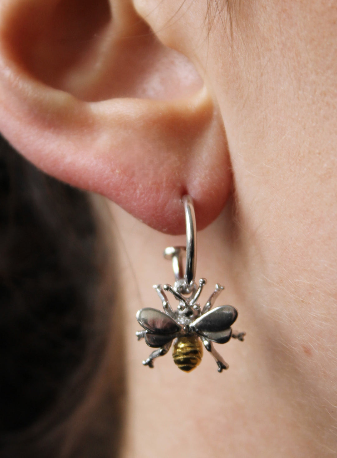 A close-up of a person's ear wearing Gallardo & Blaine Designs' Wildlife Bee Huggies (Silver or Gold), featuring a detailed hoop with a black and gold metallic bee charm.