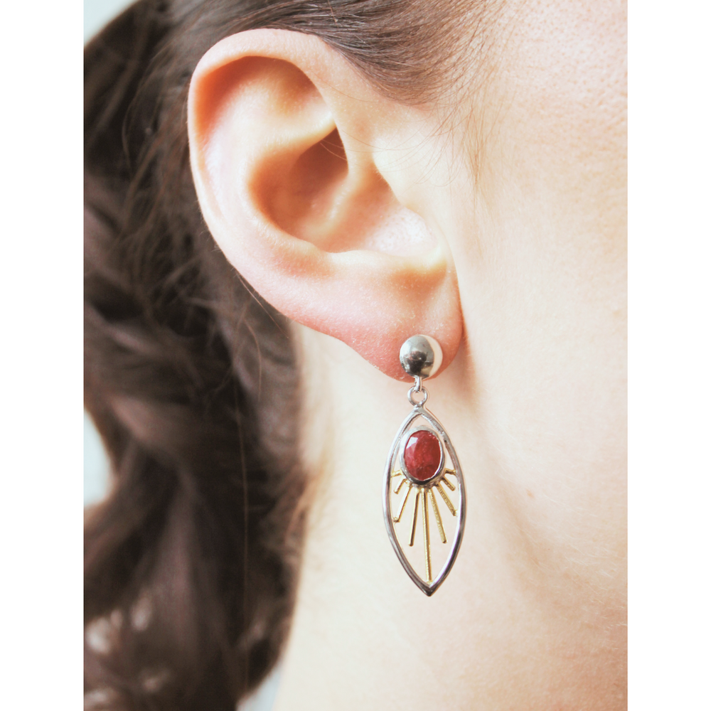 Close-up of a person wearing Gallardo & Blaine Designs’ Goddess Earrings, featuring an oval red gemstone in a leaf-shaped sterling silver frame with radiating lines. The person’s hair is pulled back to show the earring details.