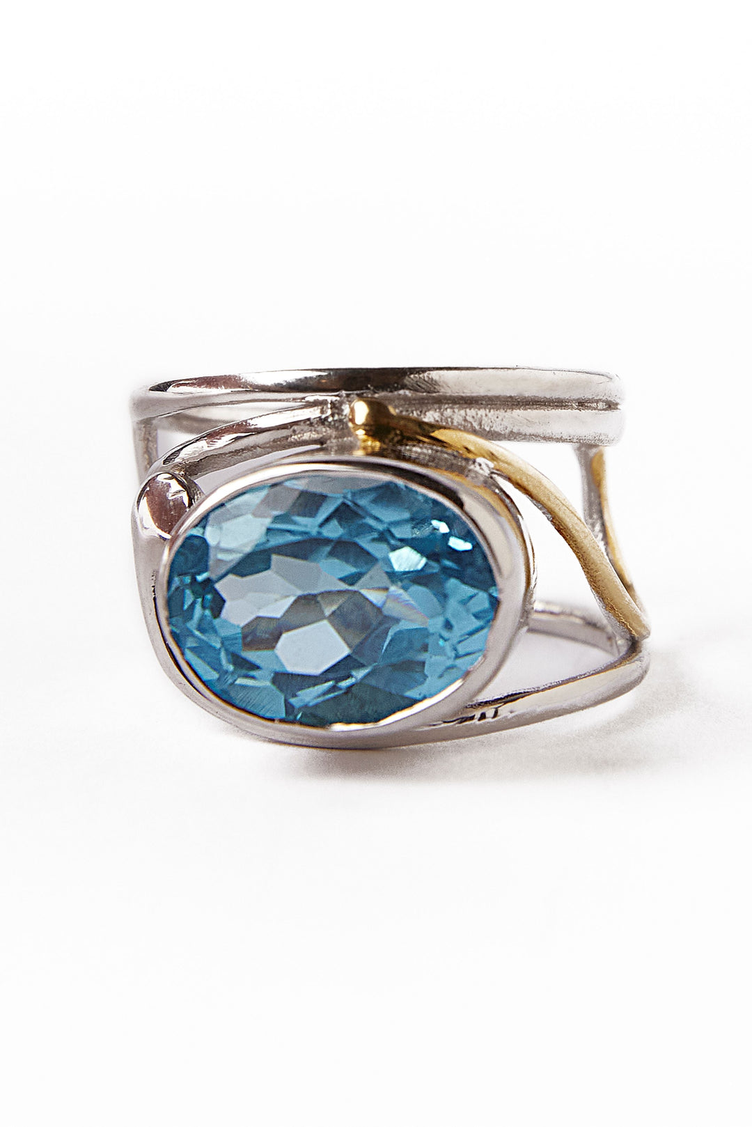 Gallardo & Blaine Designs' Horizontal Ring features an asymmetrical silver and gold band with a large oval-cut blue gemstone in the center, highlighted against a plain white background to showcase its intricate detail.