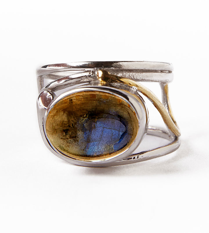 The Gallardo & Blaine Designs Horizontal Ring boasts an intricate silver and gold-plated band design with an oval labradorite gemstone. The stone's deep blue and brown hues are highlighted against a white background, showcasing the ring's detailed craftsmanship in an elegant horizontal setting.