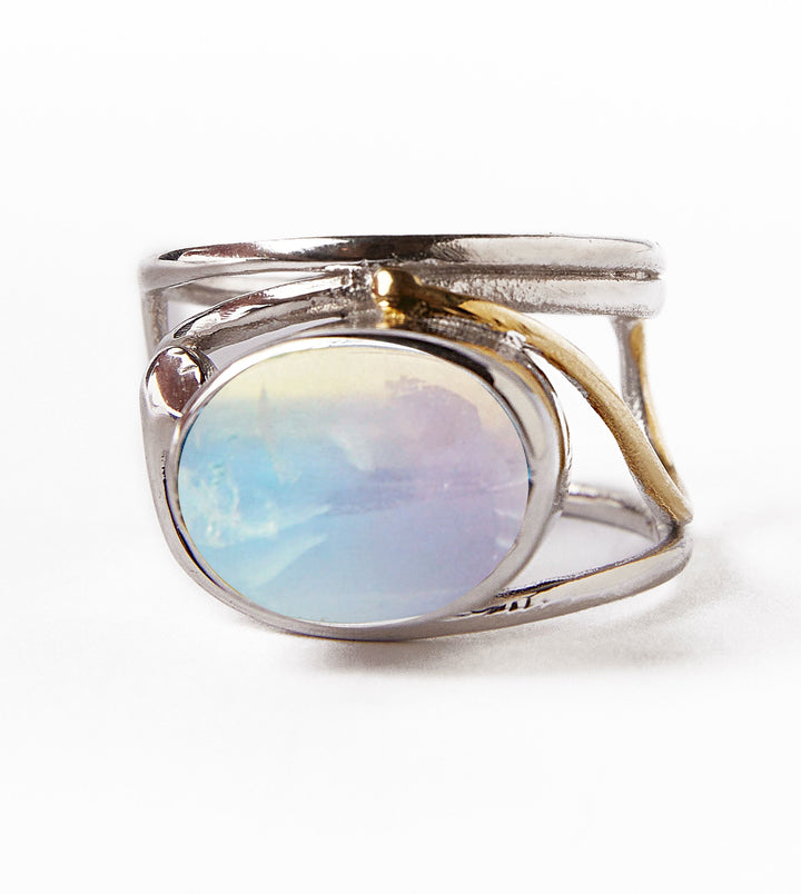 The Gallardo & Blaine Designs Horizontal Ring features a stunning oval opal gemstone with blue and cream hues, set in silver. Its unique open band is accented with a thin gold plate on one side, all showcased on a clean white background.