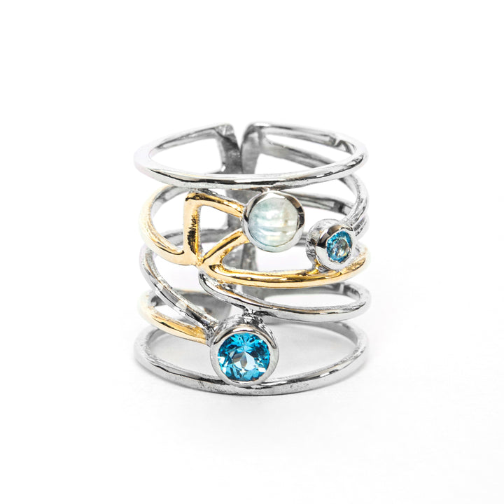 A Lattice Ring in various gemstones featuring an intricate multi-band design with gold accents, this piece showcases a contemporary design. Adorned with three gemstones: a blue gemstone at the base, a smaller blue gemstone on one side, and a round opalescent stone at the center, it perfectly blends silver & gemstones. Gallardo & Blaine Designsból