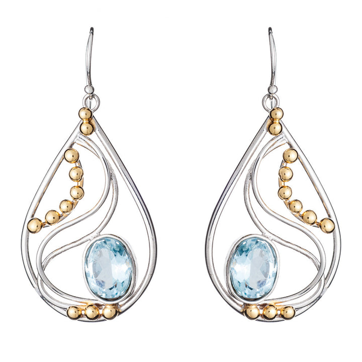 These Phoenix Earrings in various gemstones by Gallardo & Blaine Designs are a pair of elegant drop earrings featuring a combination of silver and gold elements. With a silver frame adorned with intricate swirls and small gold beads, each earring showcases a large, oval light blue gemstone at the center.
