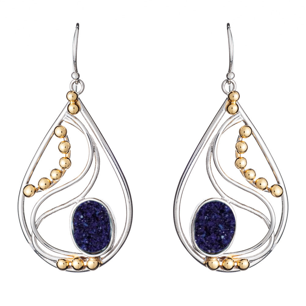 A pair of elegant drop earrings featuring silver-tone metal with curving lines and golden bead accents. The center of each Phoenix Earrings in various gemstones from Gallardo & Blaine Designs displays a deep blue oval gemstone, adding a striking contrast to the metallic elements.