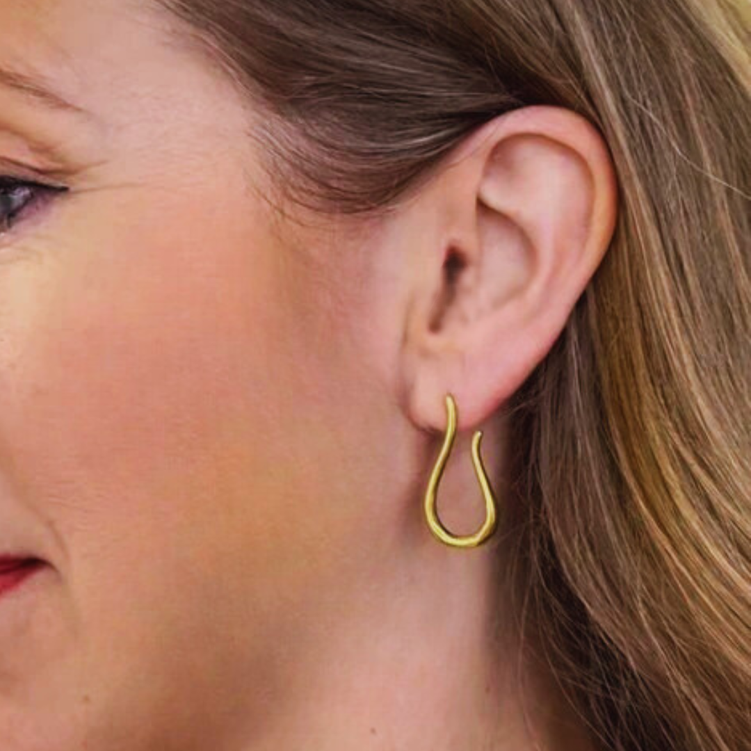 Close-up of a woman wearing Gallardo & Blaine Designs' Sea Honey Studs—gold plated silver teardrop earrings. Her light brown hair is tucked behind her ear, and she has a natural complexion with subtle makeup.