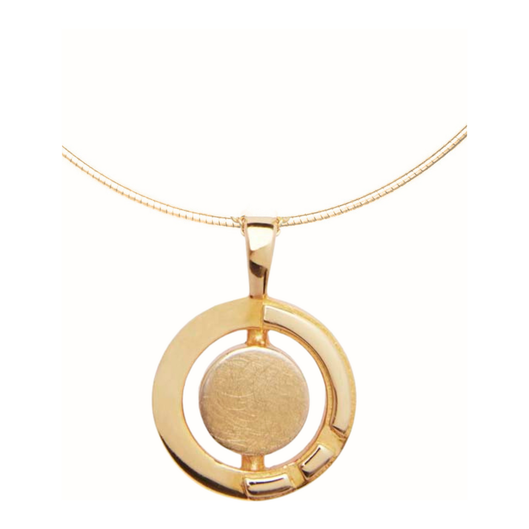 A gold vermeil necklace featuring a circular pendant. The pendant has a solid central circle enclosed within an open circular frame with a small rectangular cutout in the bottom right quadrant. Inspired by Irish heritage jewelry, the Urú Large Pendant & Chain by Gallardo & Blaine Designs features a simple gold snake chain.