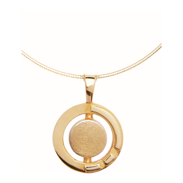 A gold vermeil necklace featuring a circular pendant. The pendant has a solid central circle enclosed within an open circular frame with a small rectangular cutout in the bottom right quadrant. Inspired by Irish heritage jewelry, the Urú Large Pendant & Chain by Gallardo & Blaine Designs features a simple gold snake chain.
