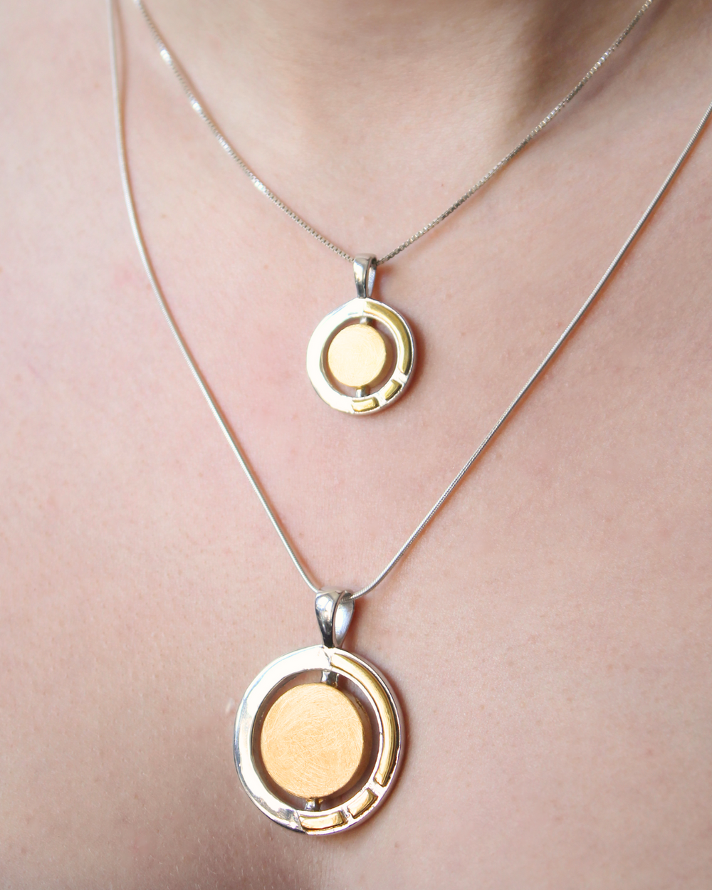 Two Gallardo & Blaine Designs Urú Small Pendant & Chain sterling silver necklaces with round gold and silver pendants—one higher, one lower—are worn together, inspired by Irish jewelry.