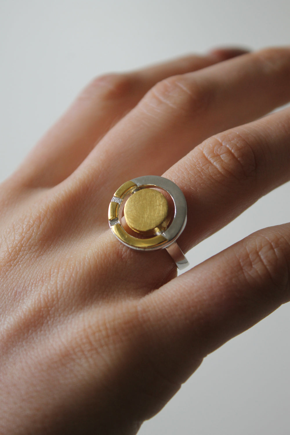 A close-up of a hand wearing the Urú Ring by Gallardo & Blaine Designs, showcasing its central gold disc and mixed metal band. The softly blurred background highlights this striking piece of modern Celtic heritage jewelry.