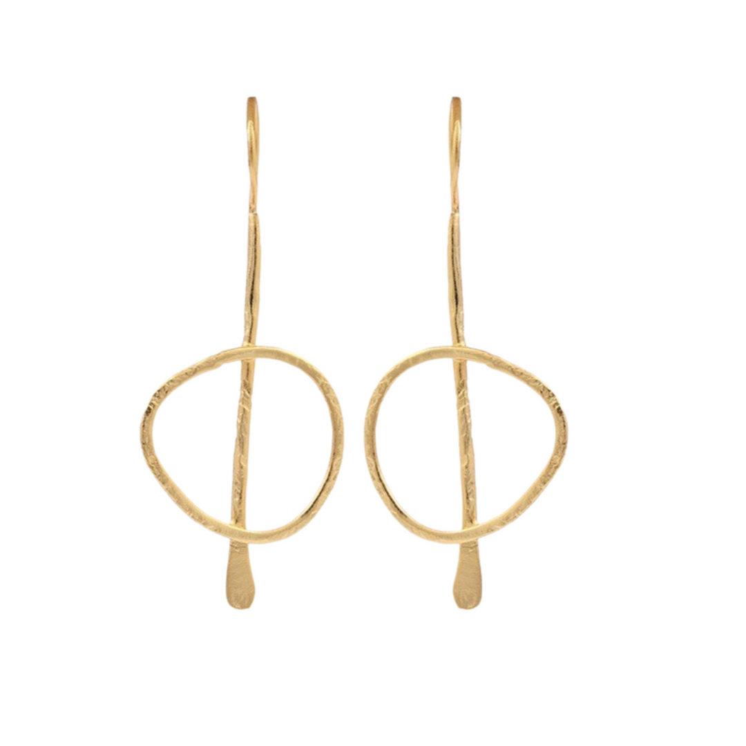 Gold plated, statement, drop earrings. The earring starts with a thin, slightly curved hook that loops through the earlobe. A slender vertical metal bar extends downward from the hook, with a slightly uneven, hand-forged texture. Attached to the vertical bar is a loosely shaped, slightly irregular circle. This frame has a hammered texture.