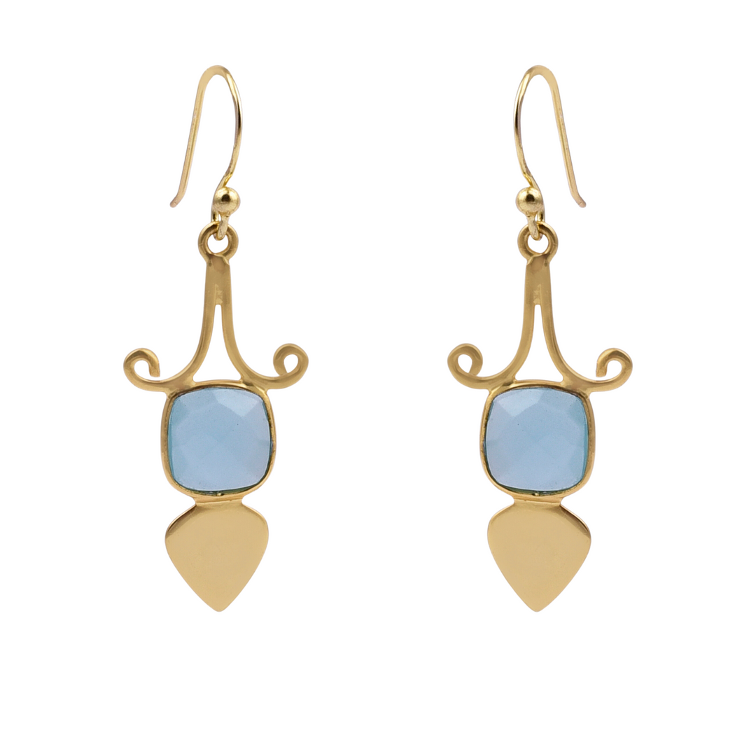 A pair of Gold Shield Aqua Chalcedony Earrings by Watermelon Tropical featuring a blue, square-cut aqua chalcedony gemstone set in an intricate gold design with swirling accents. Below the gemstone, a gold teardrop-shaped piece completes each piece of handmade jewelry.