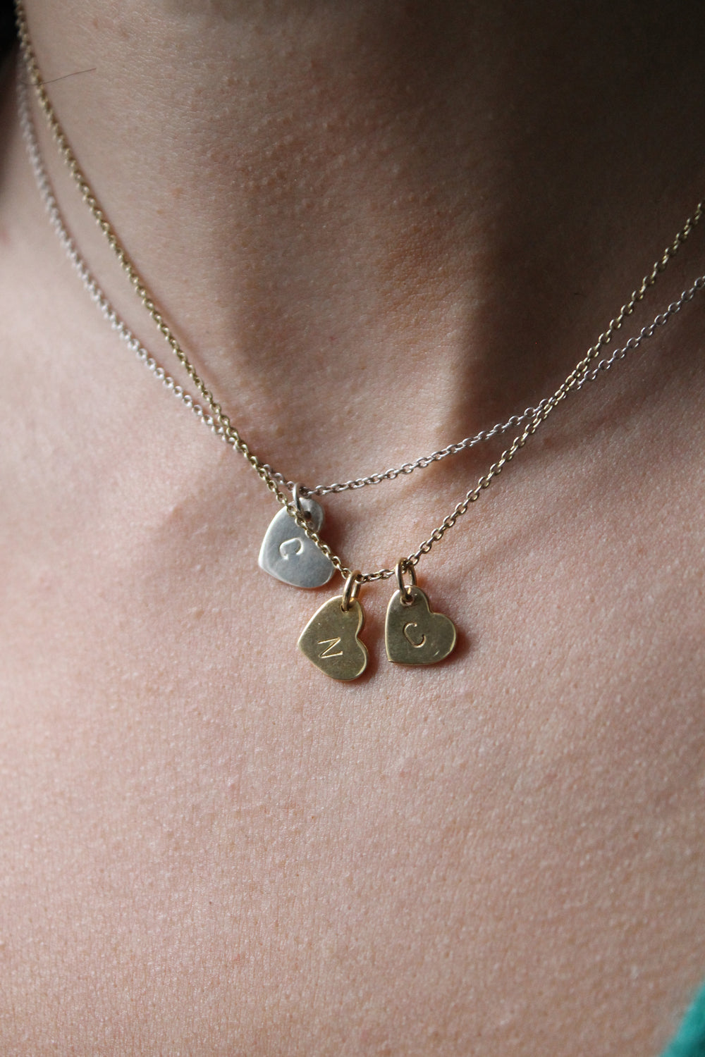 A close-up of a neck wearing three heart-shaped necklaces, featuring Personalised Charms' Personalised Large Disc Charm in Gold engraved with "Z" and "C", plus a silver pendant engraved with "C".