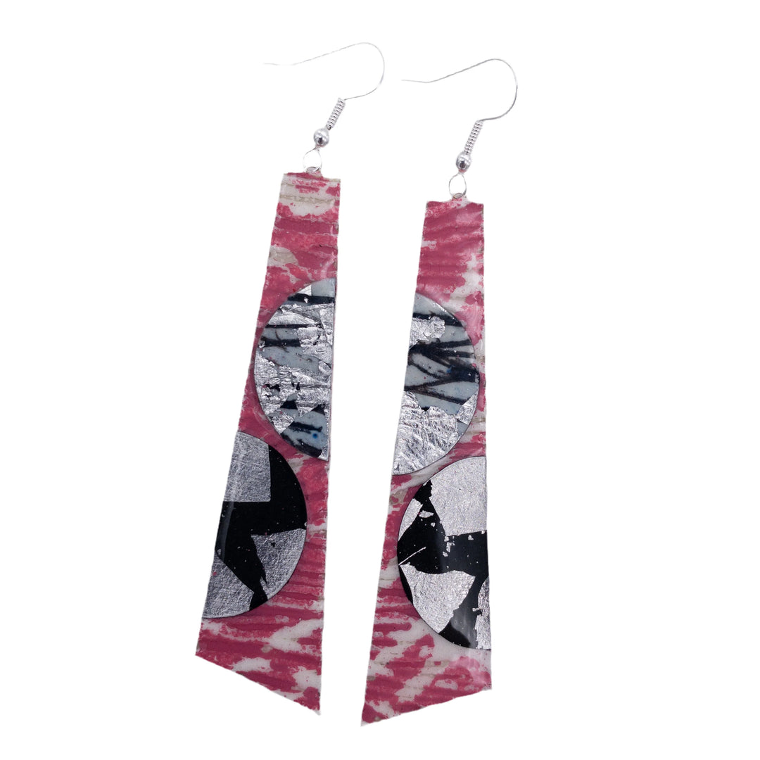 The Rothlú Hoop-La Batik Textile Earrings feature a long, triangular design in pink, grey, silver, and black with circular abstract accents and silver hooks for a unique statement look.