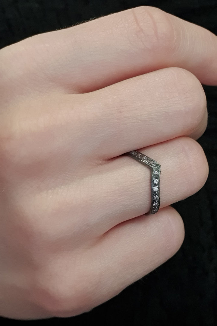 A close-up of a hand wearing the Georgia Charal Imagination Wishbone Ring, featuring a chevron-shaped sterling silver band adorned with multicoloured zircon stones, against a dark background.
