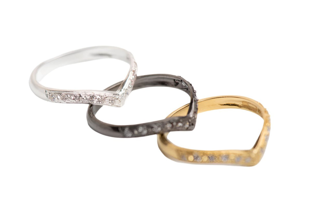 The Imagination Wishbone Ring with Zircon in various colours by Georgia Charal features three stacked V-shaped bands in silver, black, and gold tones, rhodium and gold plated, each set with sparkling zircons. Shown on a white background.
