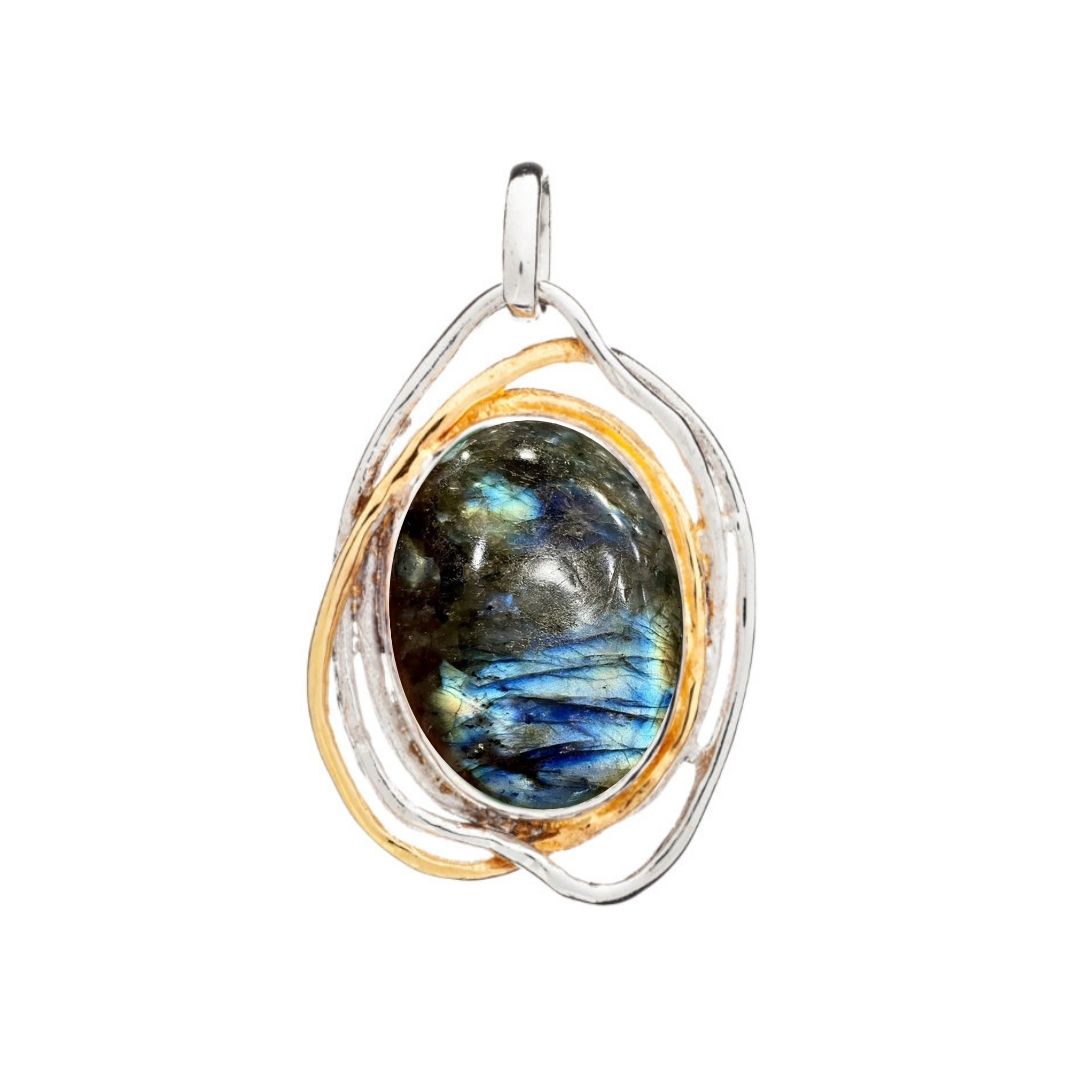 The Cosmos Pendant Large by Gallardo & Blaine Designs is a statement piece showcasing a labradorite gemstone shimmering with blue and green hues, set within an abstract silver and gold swirling dual-tone metal frame.