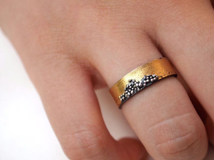 A close-up of a hand wearing the MarCucurella Narrow Etrusc Ring, crafted in 24 kt yellow gold and oxidized silver, featuring textured bands and a cluster of small raised beads in an Etruscan-inspired design.