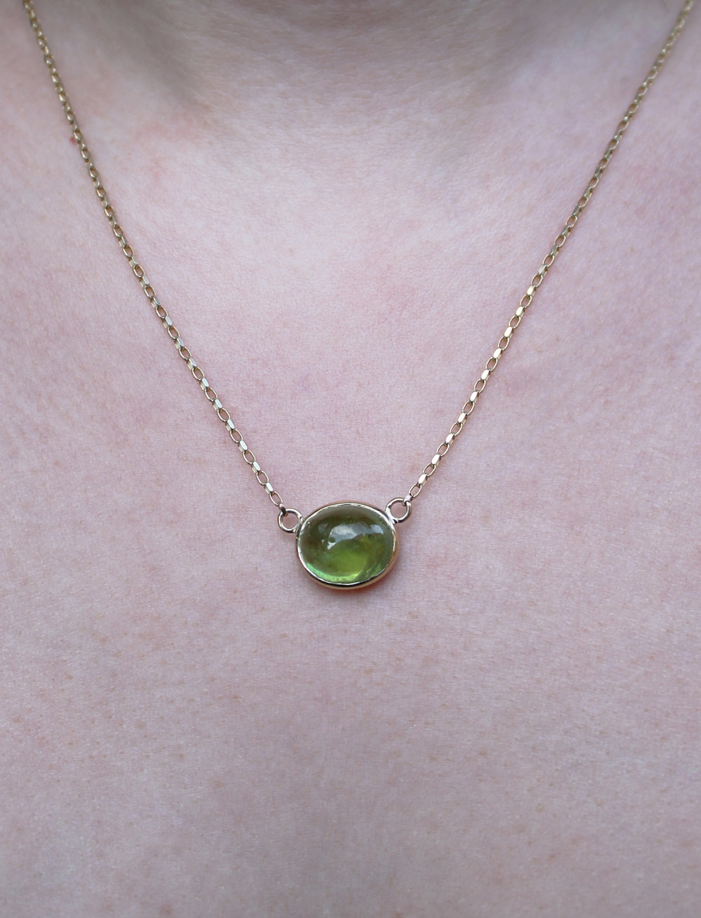 A close-up of the Madeleine Whispering Moss 9ct Yellow Gold Necklace, featuring a round green gemstone pendant, worn around the neck.