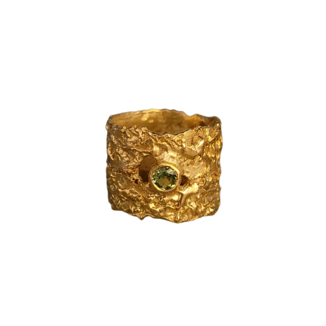 The 'That Place Beyond' Wide Ring by Caroline Stokesberry-lee is crafted in 18ct gold plate with a textured organic surface, set with a round green gemstone at the center.