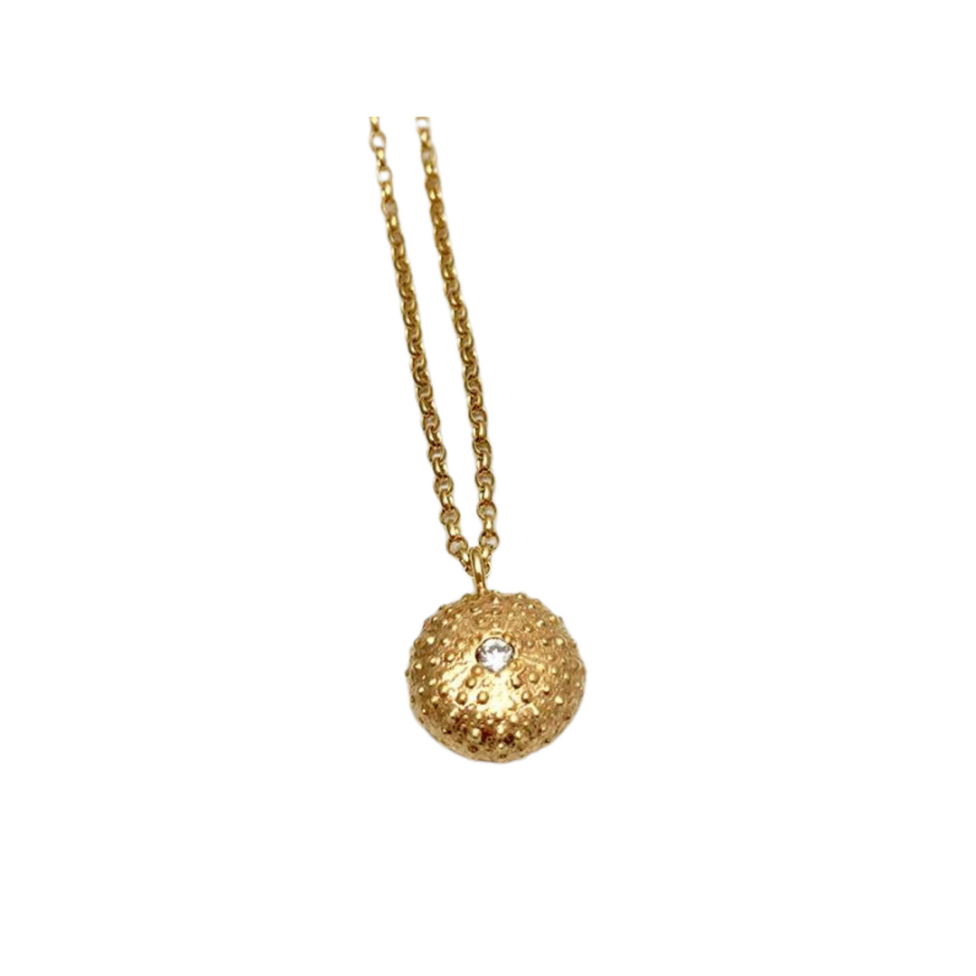 The Jennifer Kinnear Sea Urchin Necklace with Stone features a textured round pendant with a clear gemstone center on a simple gold or silver chain, shown against a white background.
