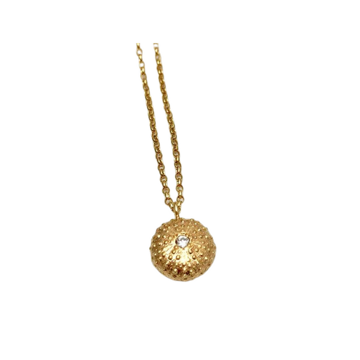 The Jennifer Kinnear Sea Urchin Necklace with Stone features a textured round pendant with a clear gemstone center on a simple gold or silver chain, shown against a white background.