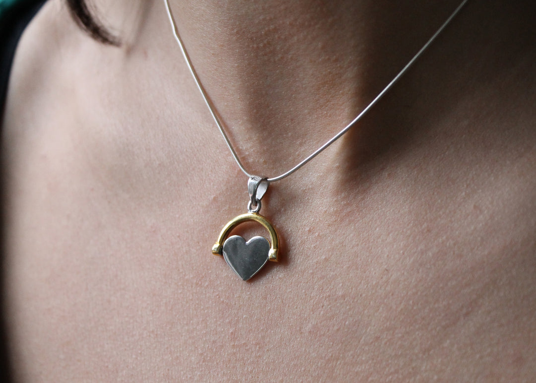 A close-up of Engravable Jewellery's Gold Plate Spinning Heart necklace, featuring a customizable heart-shaped pendant with a gold arc, worn around someone's neck.