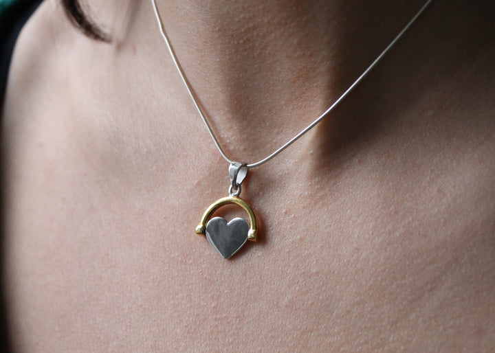 A close-up of Engravable Jewellery's Gold Plate Spinning Heart necklace, featuring a customizable heart-shaped pendant with a gold arc, worn around someone's neck.