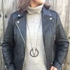 A person wearing a black leather jacket over a gray turtleneck sweater styles the Elsiem Vibe Pendulum Necklace, standing in front of a wooden fence.