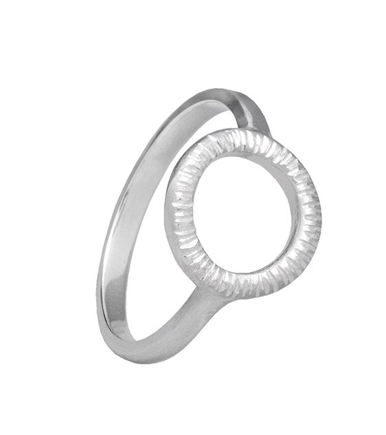 The Aud Into The Light Mini Ring Silver is a handmade, sterling silver ring featuring a unique design with a circular, textured open center. The ring band is smooth and sturdy, providing a modern and elegant appearance.