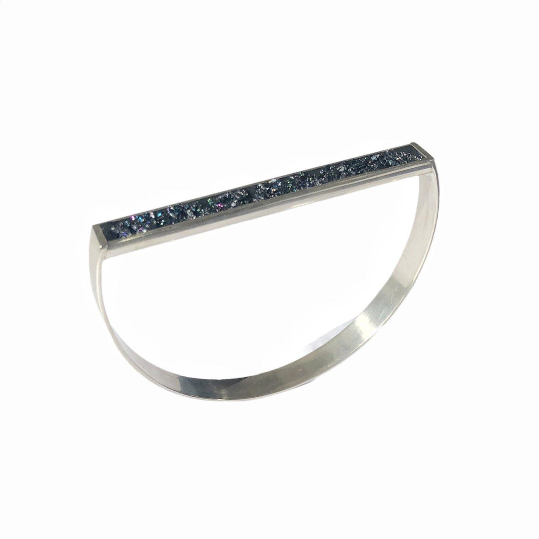 A sleek, modern Urban Geode Bangle by Angela O'Keefe featuring a unique flat top adorned with a row of small, sparkling blue gemstones. The bracelet has a minimalist design with a curved, open style and a polished finish.