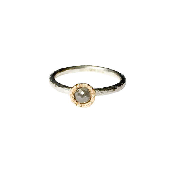 A minimalist ring featuring a single, round grey diamond set in a textured gold bezel on a slim, hammered finish sterling silver stacking ring. The Aurous Ring Silver Grey Diamond by Abbie Dixon is placed against a plain white background.