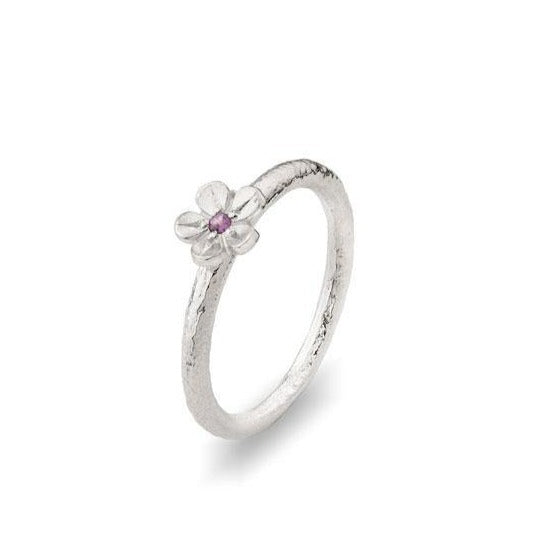 A delicate handmade sterling silver ring featuring a small flower with a single pink garnet at its center. The Fiona Kerr Cherry Blossom Small Silver Ring With Garnet (Size 7 x 2mm) has a textured, rustic finish, giving it an artisanal appearance. The flower sits atop the thin band, adding a touch of elegance to the simple design.