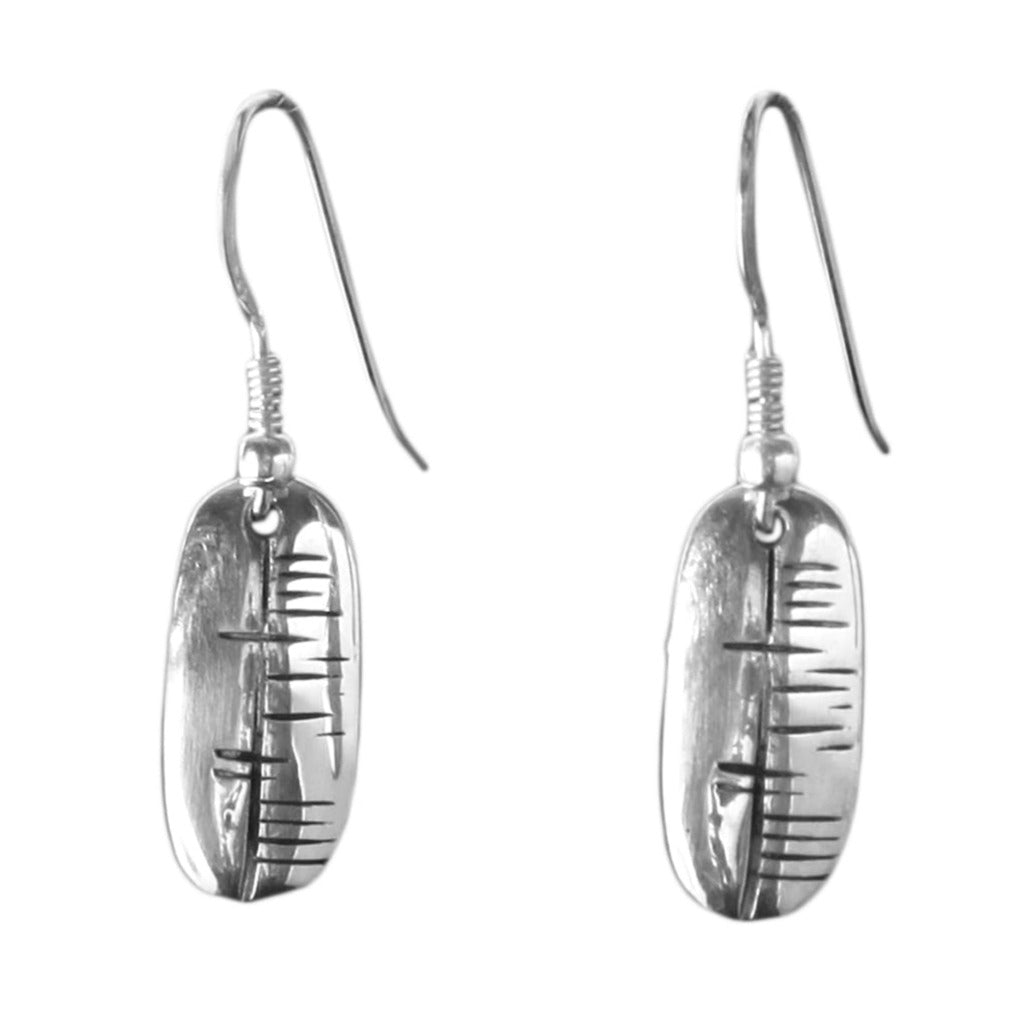 The Happiness (Sonas) Carved Earrings by Ogham Treasure are sterling silver earrings featuring vertically oriented oval pendants with inscribed linear patterns reminiscent of ancient ogham tally marks. The design exudes a blend of modern and rustic aesthetic, embodying a touch of Irish happiness.