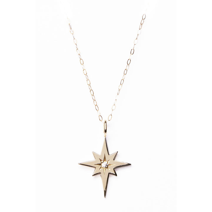 The Diamond Polaris Pendant by Cosmic Boulevard is a minimalist necklace featuring a delicate chain and a pendant shaped like a compass star with a small diamond in the center. The gold-toned or sterling silver chain has evenly spaced links, adding to the elegance of this handmade jewellery piece.
