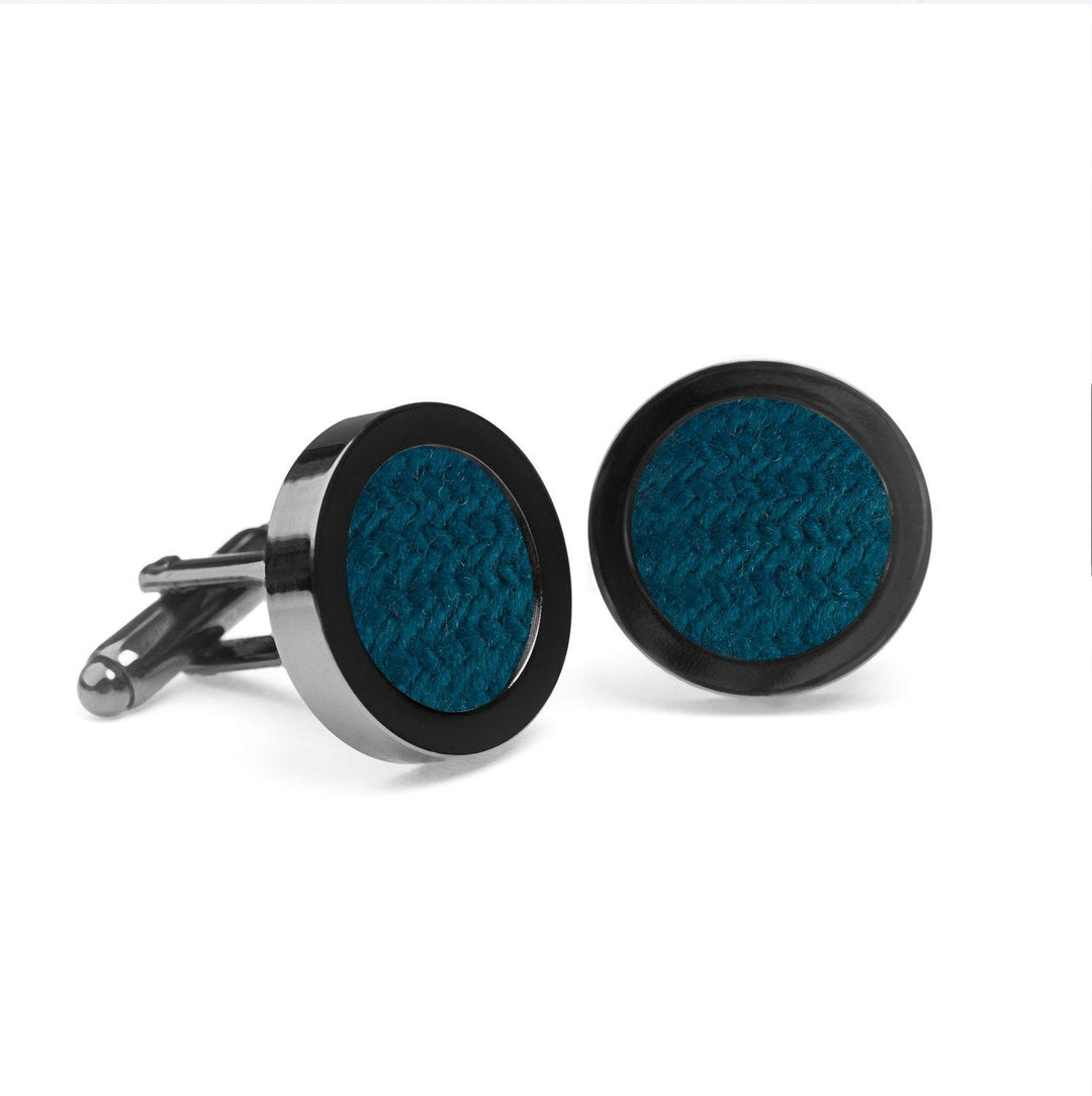 A pair of Teal Tweed Cufflinks from Orwell & Browne with a sleek silver finish, each featuring a dark blue textured center reminiscent of Donegal tweed. The cufflinks are positioned upright on a plain white background, showcasing their elegant design.