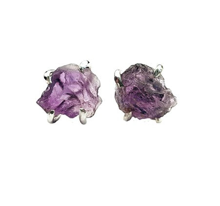 A pair of Raw Amethyst Studs by Caroline Stokesberry-lee featuring raw amethyst gemstones in irregular shapes set on sterling silver ear posts. The amethysts are a light, translucent purple, showcasing their natural, unpolished form.